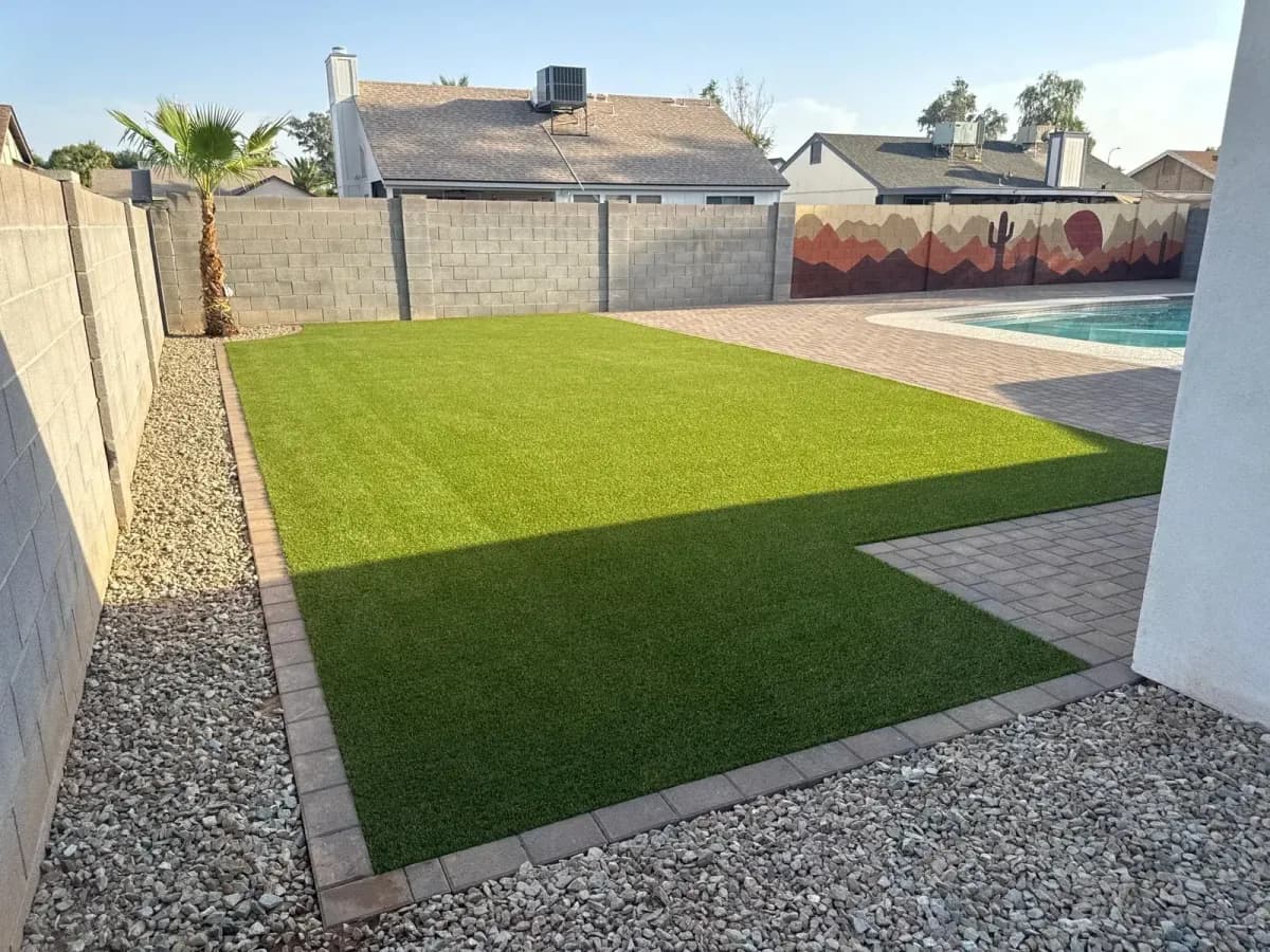 The same backyard after, with artificial turf, paver borders and clean lines